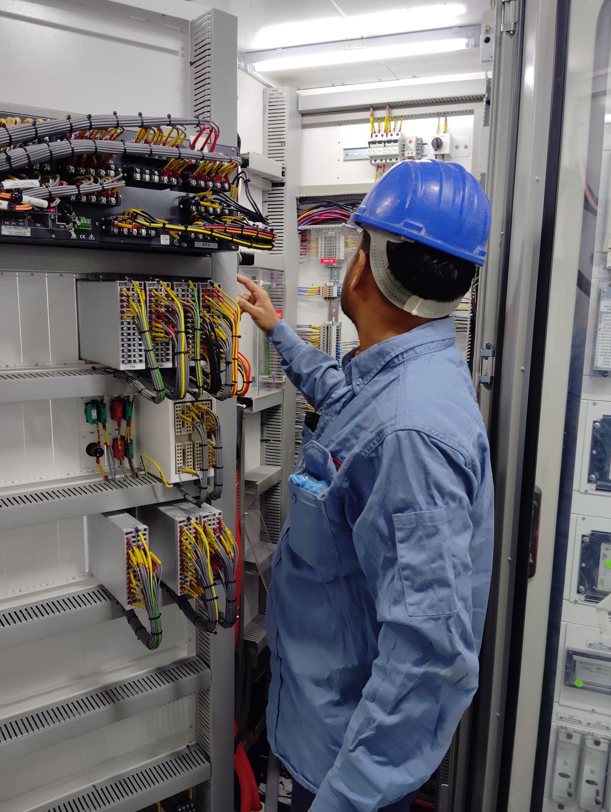 Electrician in a hard hat inspecting an industrial control panel