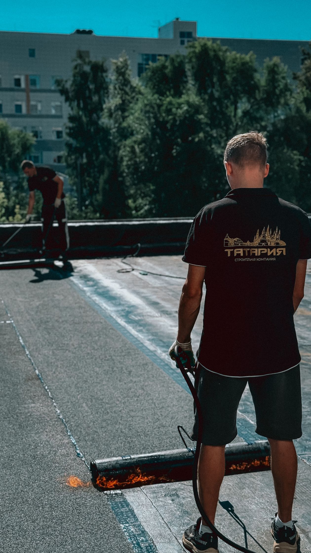 Roofers applying hot bitumen to a flat roof